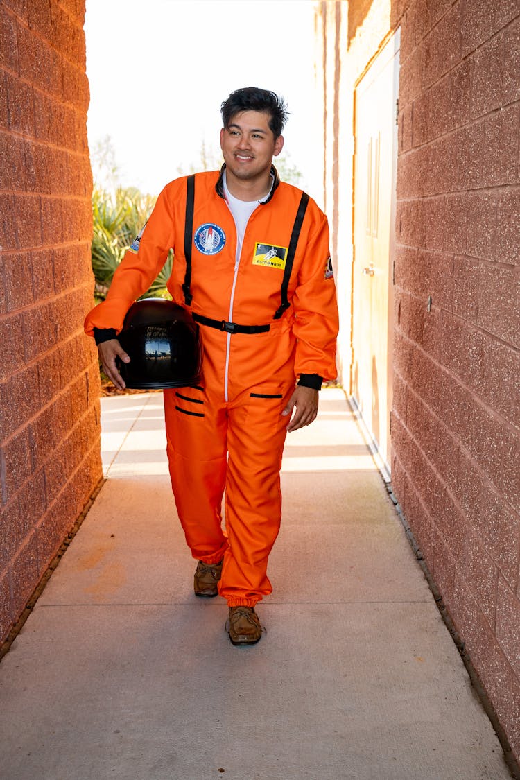 Man In Orange Work Uniform Walking Through Narrow Alley