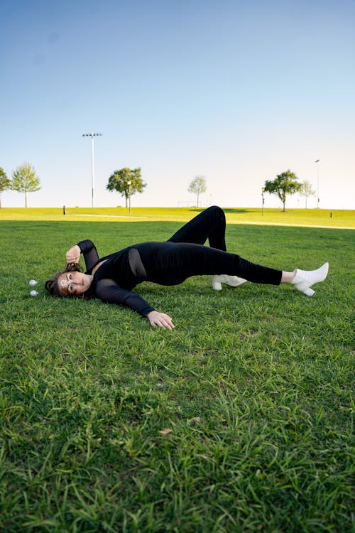 Woman in Black Long Sleeve Shirt and Pants Lying on Green Grass Field