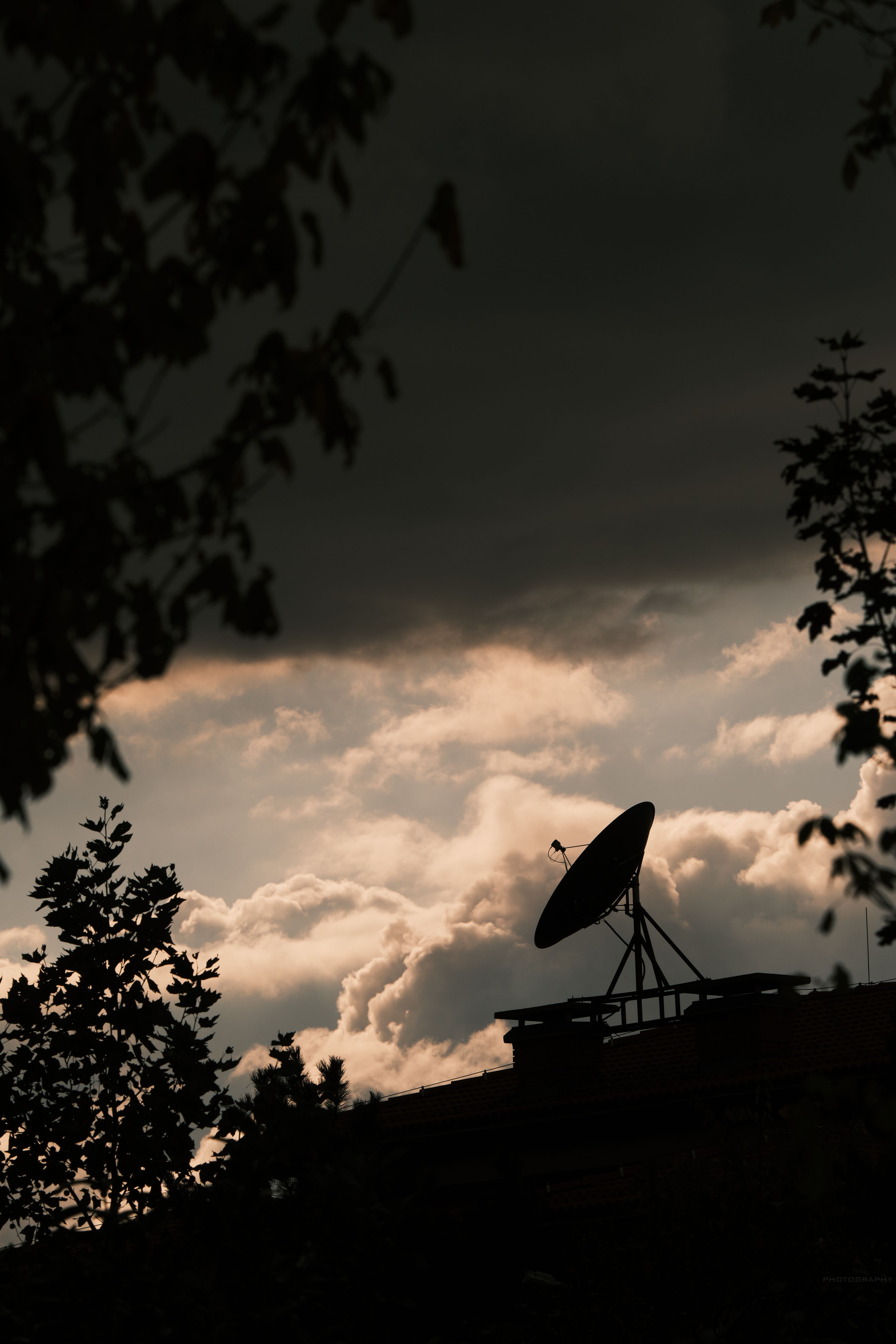 Silhouette of a satellite dish against a dramatic twilight sky with clouds