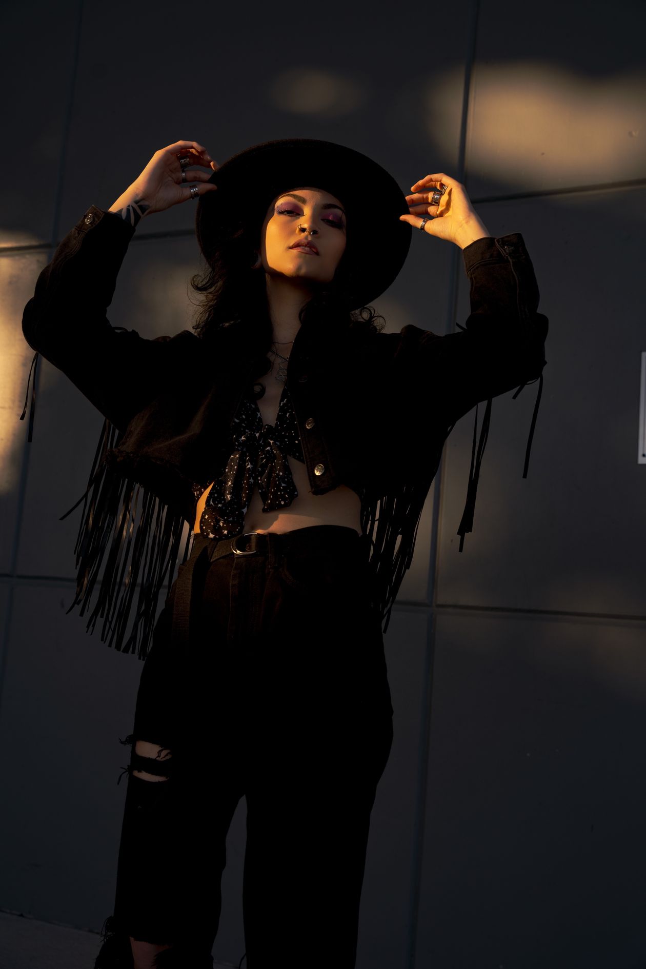 Woman in a black fringe jacket and wide black hat in golden evening light