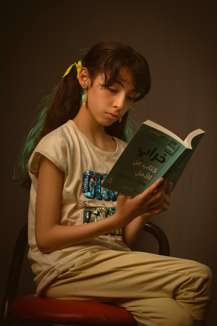 Girl Sitting On Chair While Reading A Book