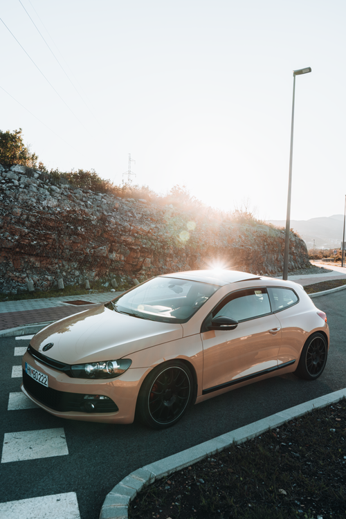 Free Shiny hatchback car parked on a road with sun flare, in a scenic Montenegro setting. Stock Photo