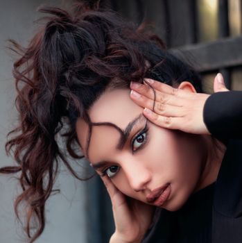 Close-up portrait of a fashionable woman posing with hands on her face.