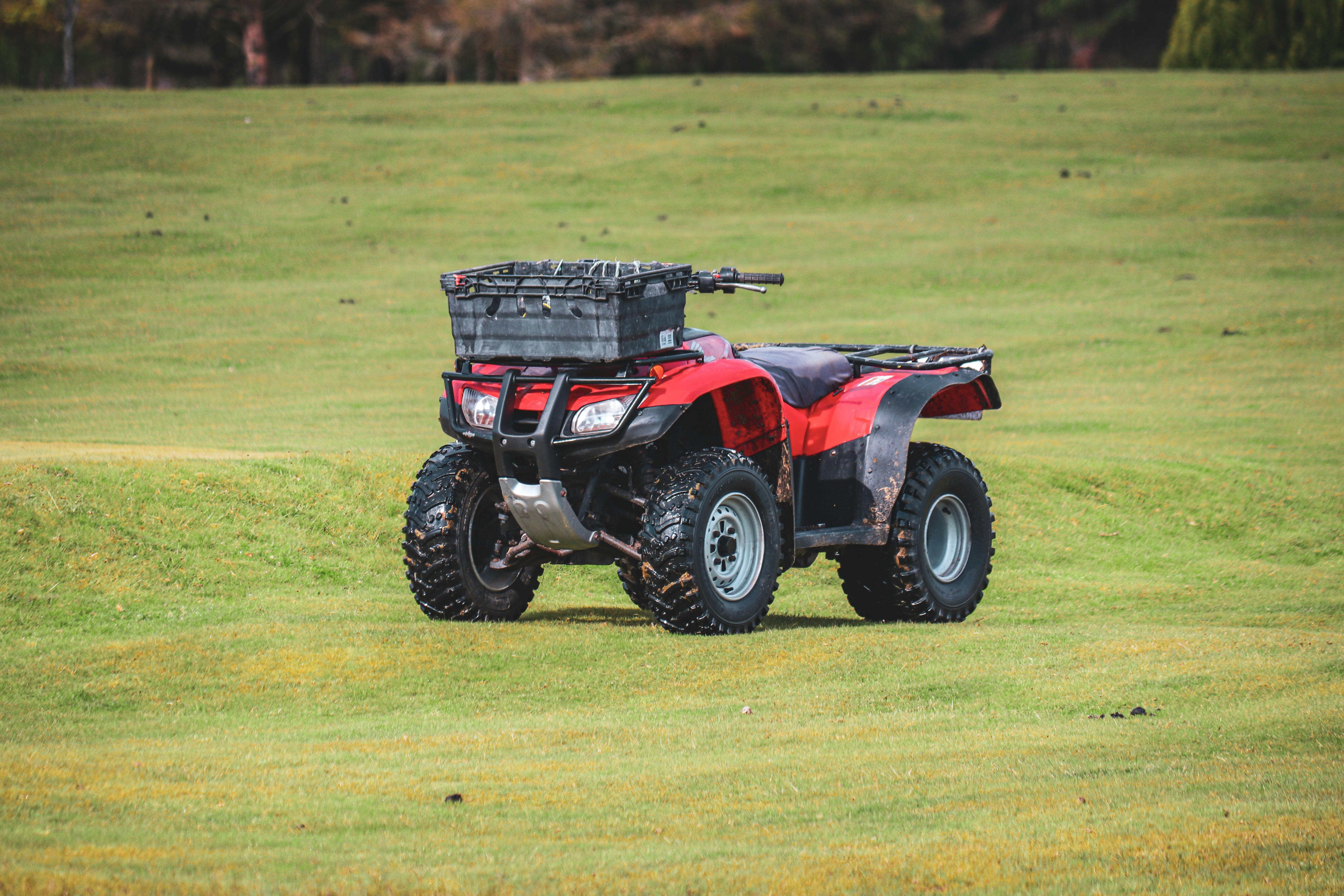 Red all-terrain vehicle parked in a vibrant green field in the countryside, perfect for adventurous travel.