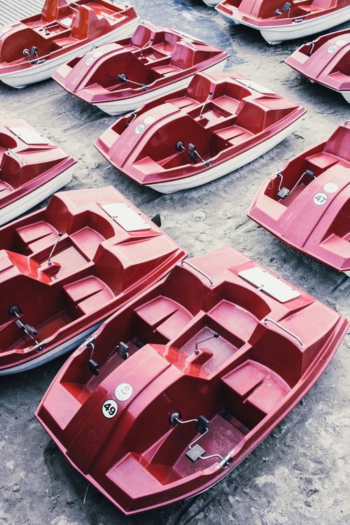 Free Row of vibrant red pedal boats neatly arranged on a sandy surface, ready for use. Stock Photo