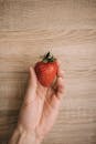 木制背景下，一只手拿着新鲜成熟草莓的特写