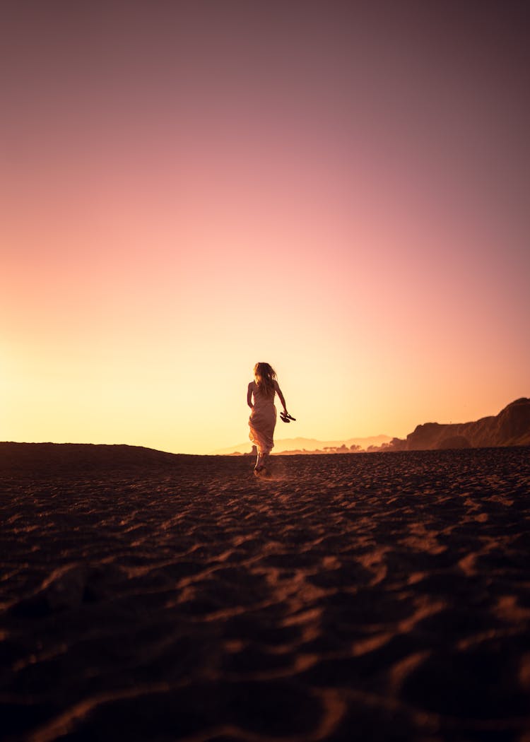 Woman In Dress Walking Alone On Beach At Sunset