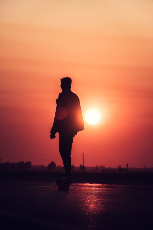 Free A dramatic silhouette of a man skateboarding against a vibrant sunset sky. Stock Photo