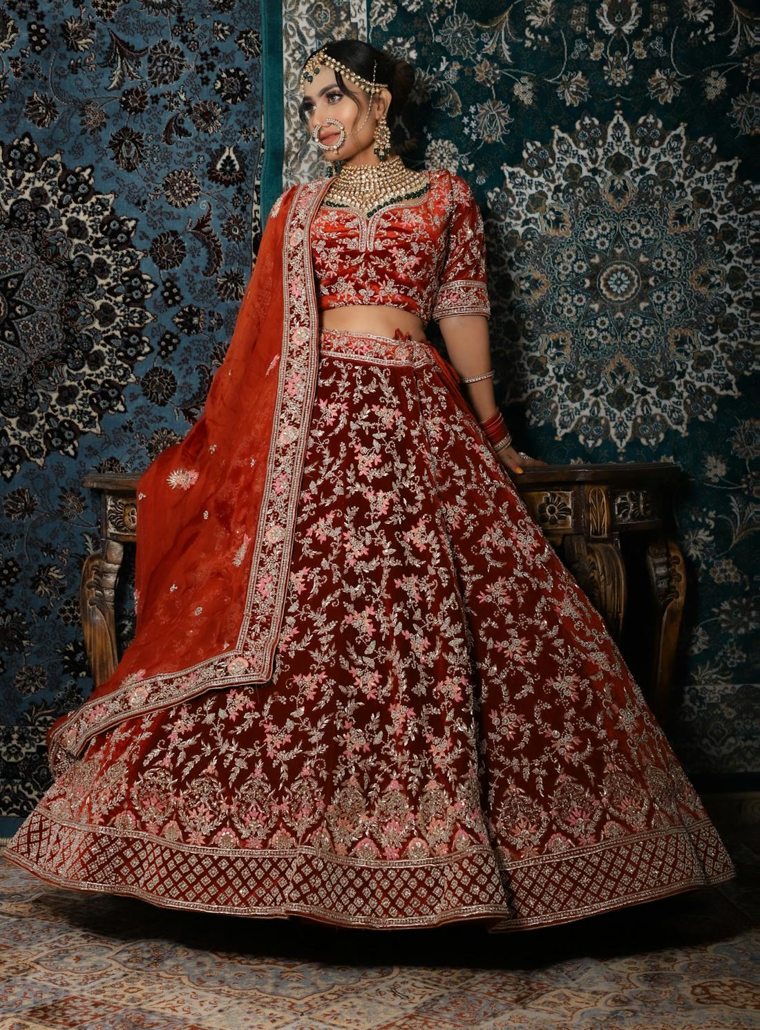 Bride posing indoors in a deep maroon lehenga with a flowing dupatta cape
