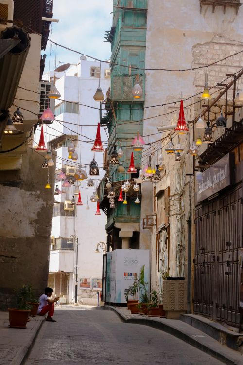 Free A picturesque alleyway adorned with hanging lanterns and a person seated, capturing urban tranquility. Stock Photo