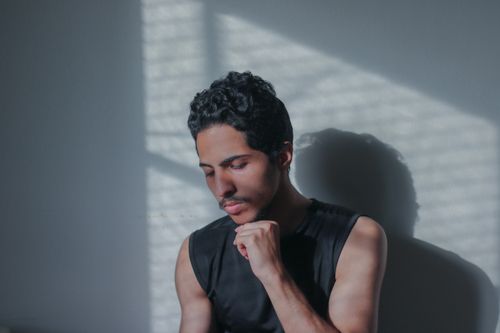 Free A man with a thoughtful pose, highlighted by striking shadows on a wall. Stock Photo