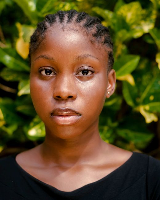 A thoughtful and serene close-up portrait of a young black woman against lush green foliage.