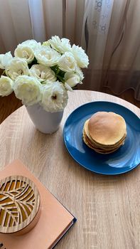 A serene breakfast scene featuring pancakes and white roses in a vase on a wooden table.