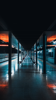 A striking empty railway platform at night, illuminated by neon signage and reflections.