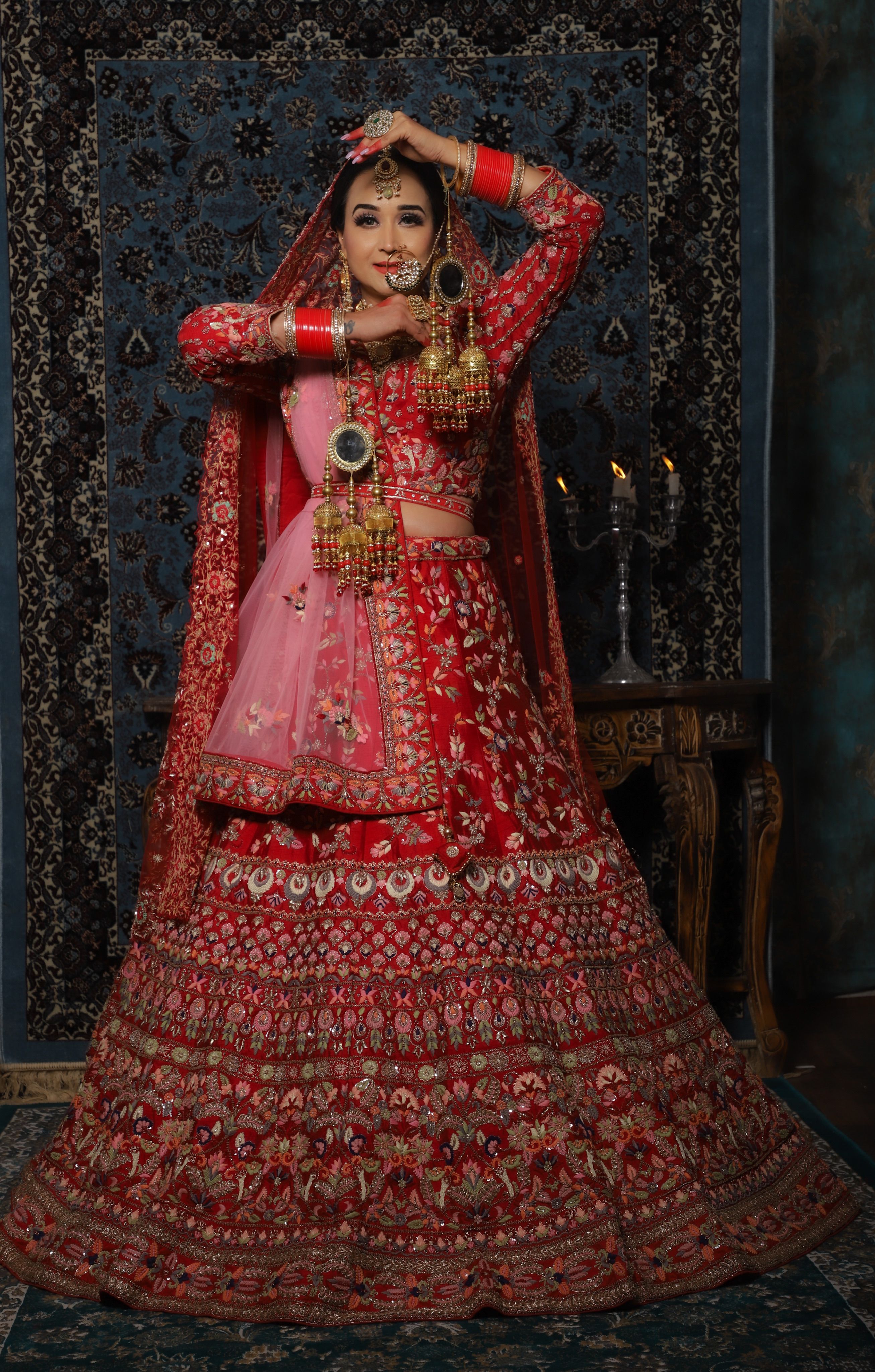 Elegant Indian bride in classic red bridal lehenga posing gracefully indoors.