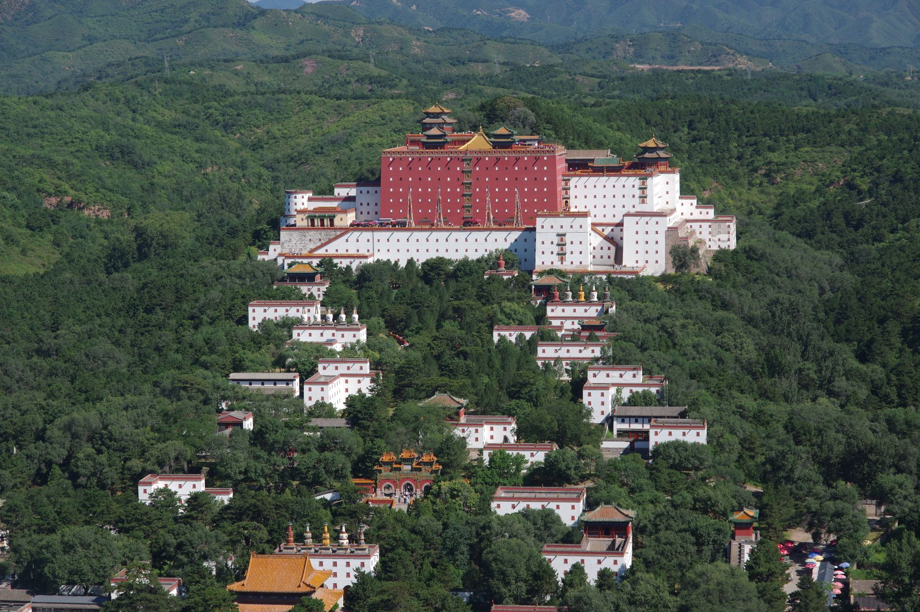 Aerial view of a temple complex nestled in lush green hills under a clear sky.