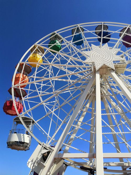 Free Vibrant Ferris wheel with colorful cabins against a clear blue sky in Barcelona. Stock Photo