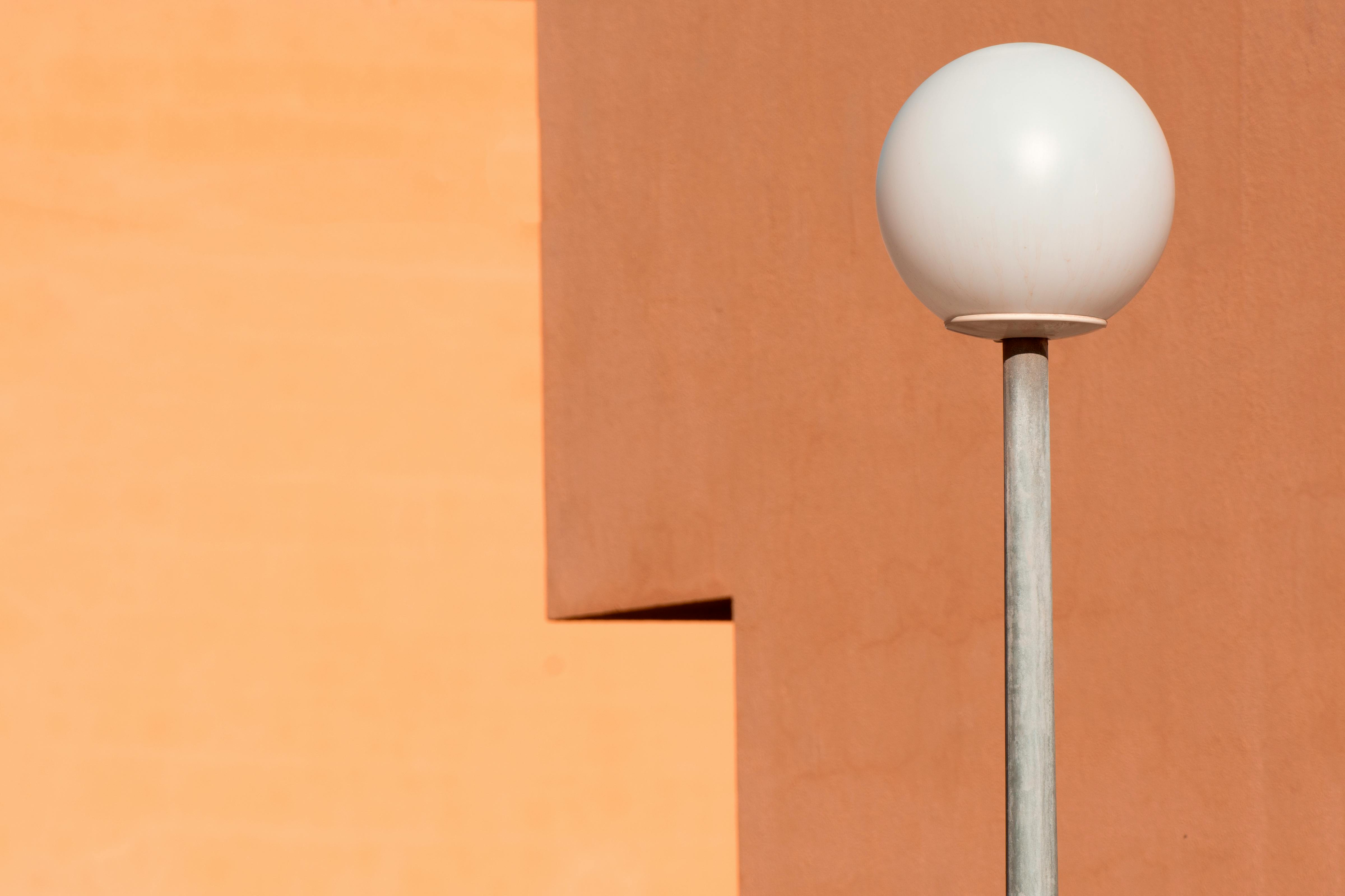 A modern streetlamp stands out against a vibrant orange wall, exemplifying minimalist design.