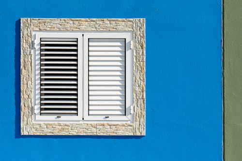 Free Close-up of a shuttered window on a vibrant blue wall with stone trim. Stock Photo