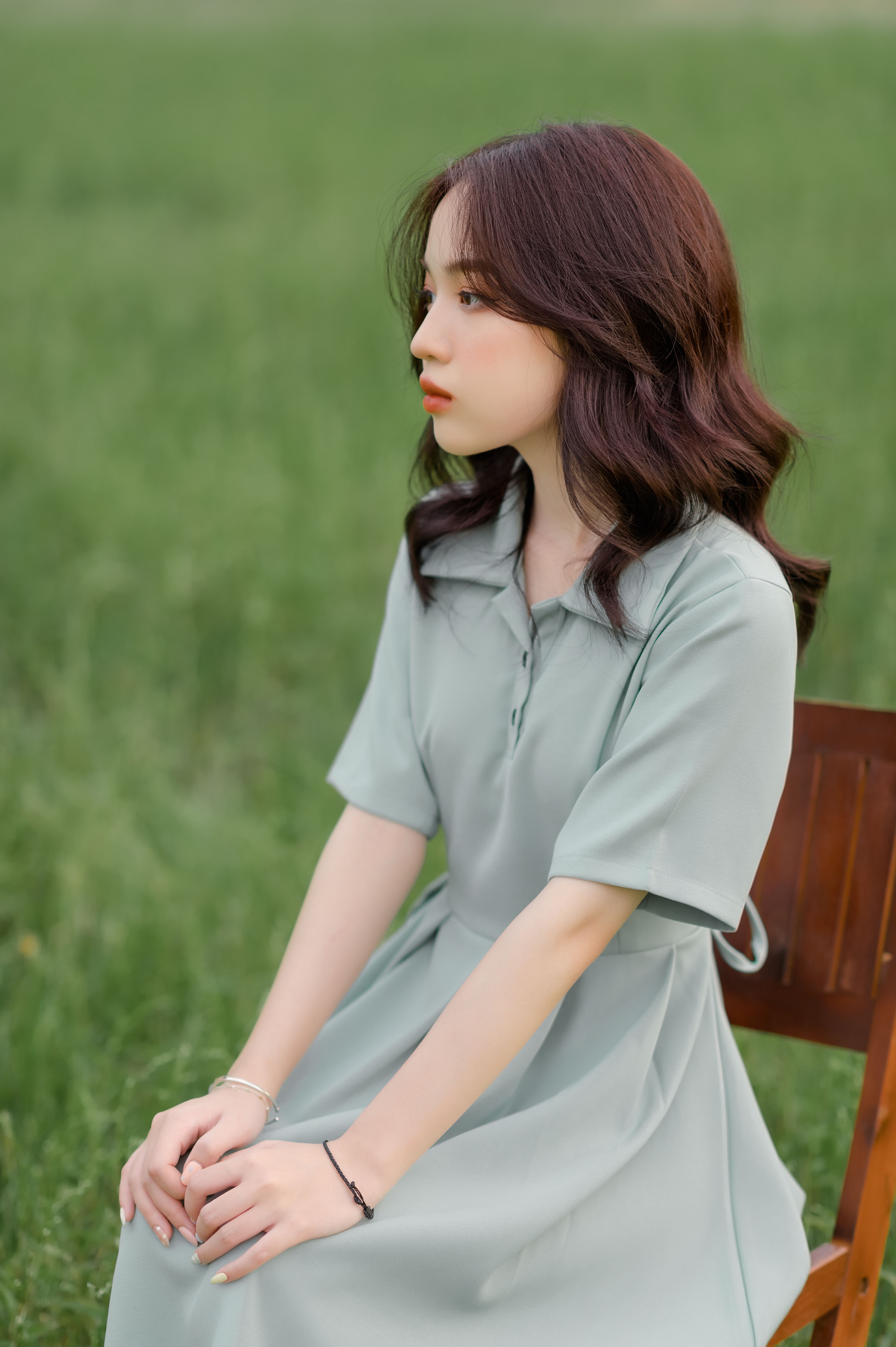 Portrait of a young woman seated outdoors in a green dress on a wooden chair in Vietnam.