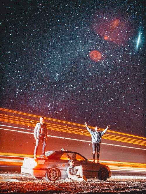 Free Three people atop a car under a vivid starry sky in Morocco's desert night. Stock Photo
