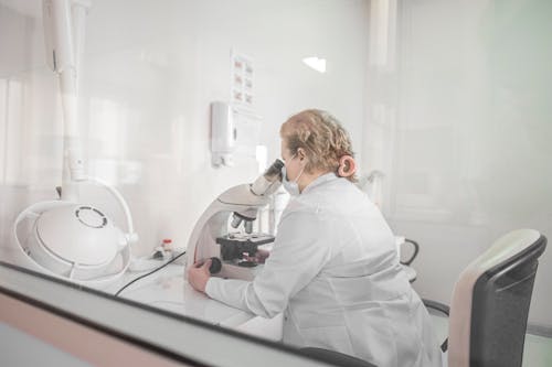 Woman in White Robe Looking Through Microscope