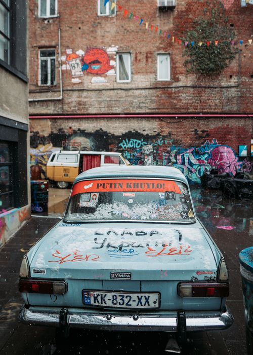 Free A vintage car with graffiti in a vibrant Tbilisi courtyard, surrounded by street art. Stock Photo