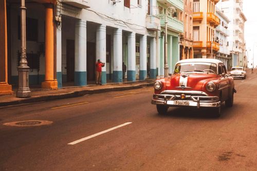 Free Classic car drives through colorful Havana street, capturing Cuban charm. Stock Photo