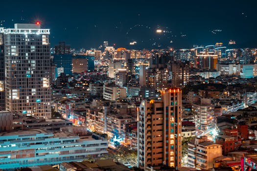 A vivid aerial cityscape featuring glowing urban lights and towering buildings at night.