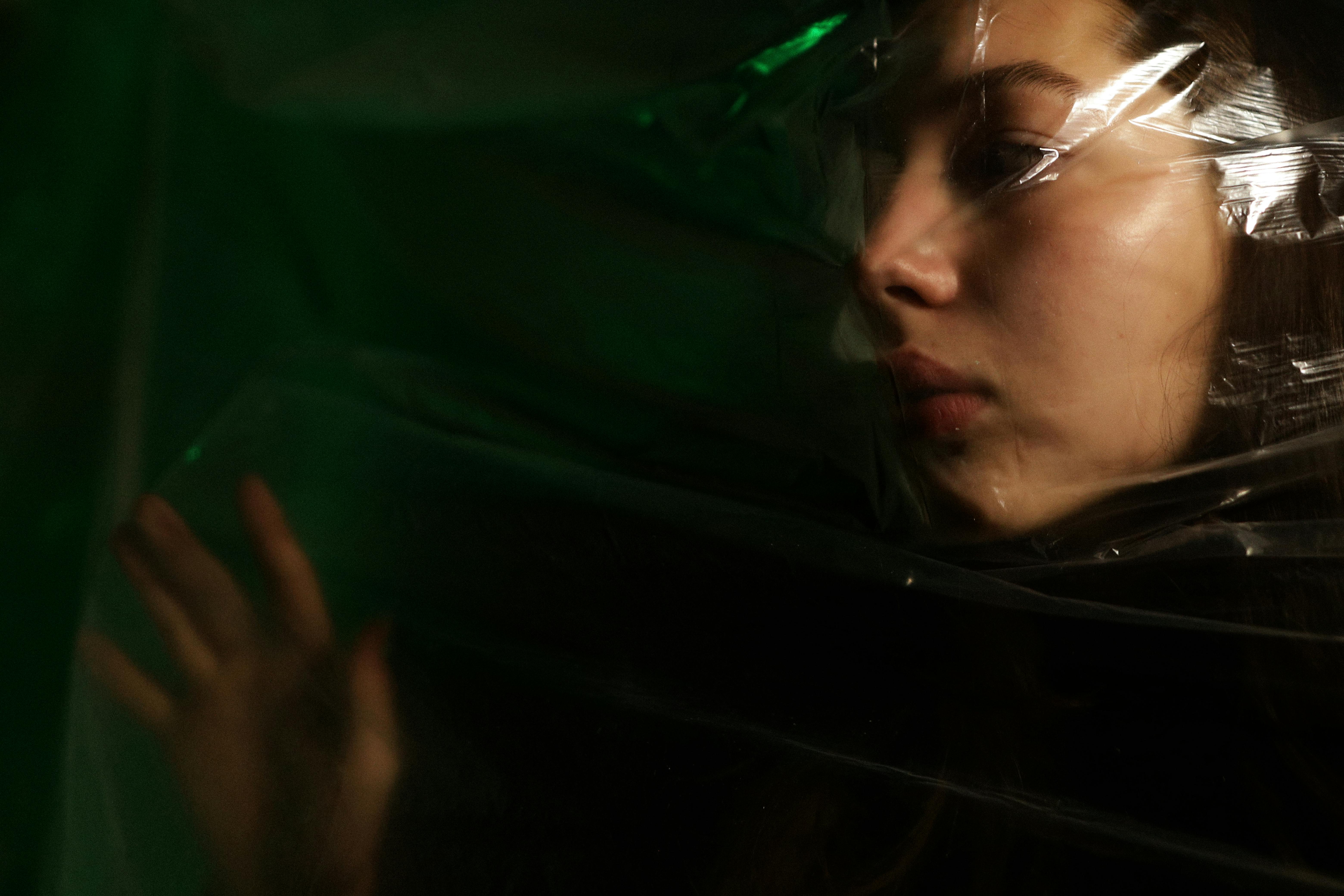 Artistic portrait capturing moody expressions through plastic barrier.