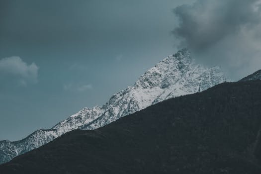 Snow-capped mountain peak against a cloudy sky, offering a dramatic natural landscape view.