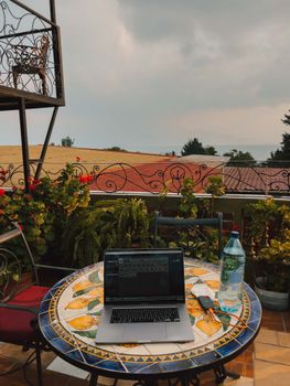 A cozy balcony setup featuring a laptop on a table with plants and a scenic city view.