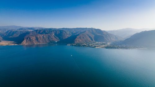Free A breathtaking aerial view showcasing a tranquil lake surrounded by mountains under a clear blue sky. Stock Photo