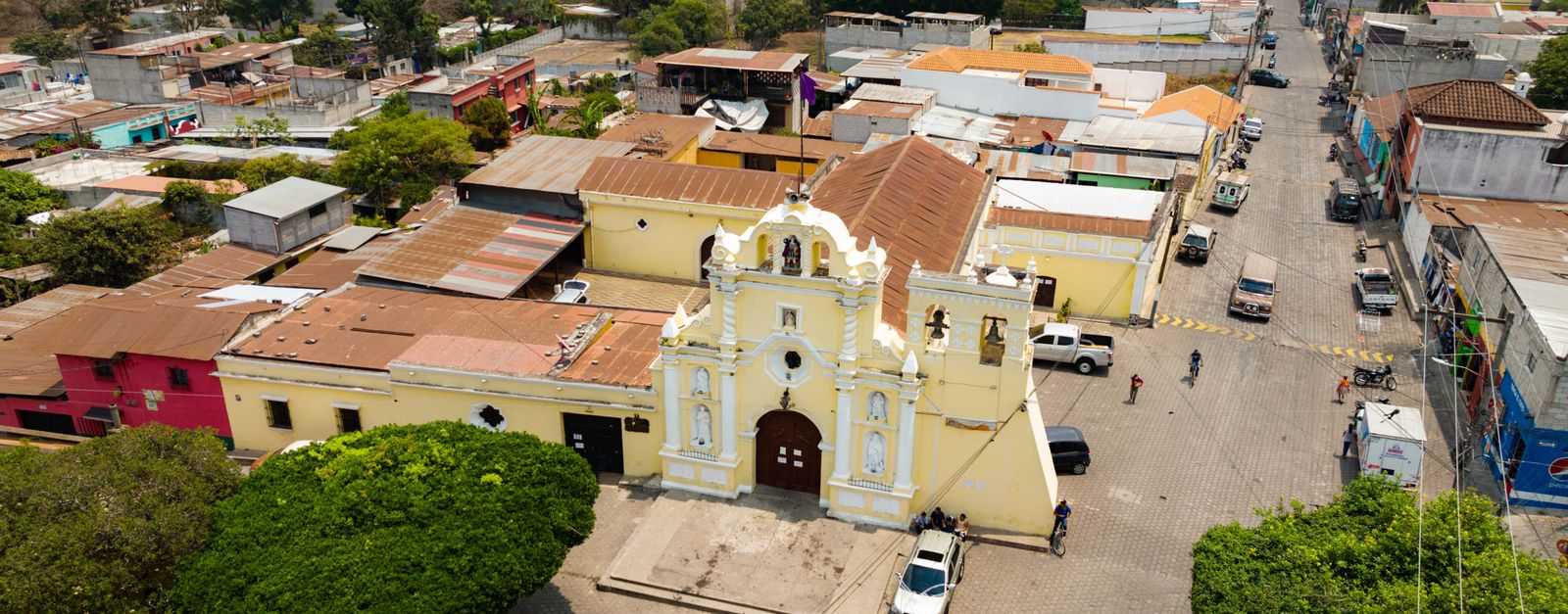 Captivating aerial view of a historic church in a vibrant Guatemalan town, showcasing colorful buildings.