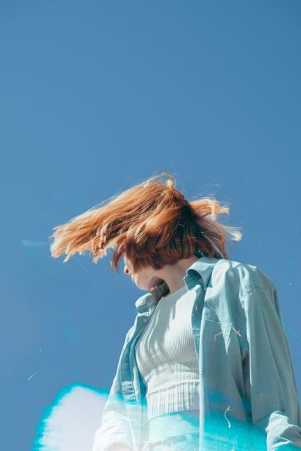 A woman in flowing blue attire captured dynamically against a clear sky, exuding energy and freedom.