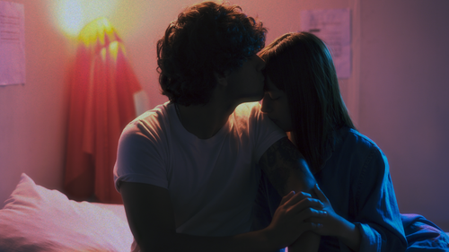 Free A young couple sharing a tender moment indoors with a warm, intimate ambiance. Stock Photo