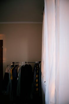 A cozy interior features clothes hanging on a rack with sunlight filtering through curtains.
