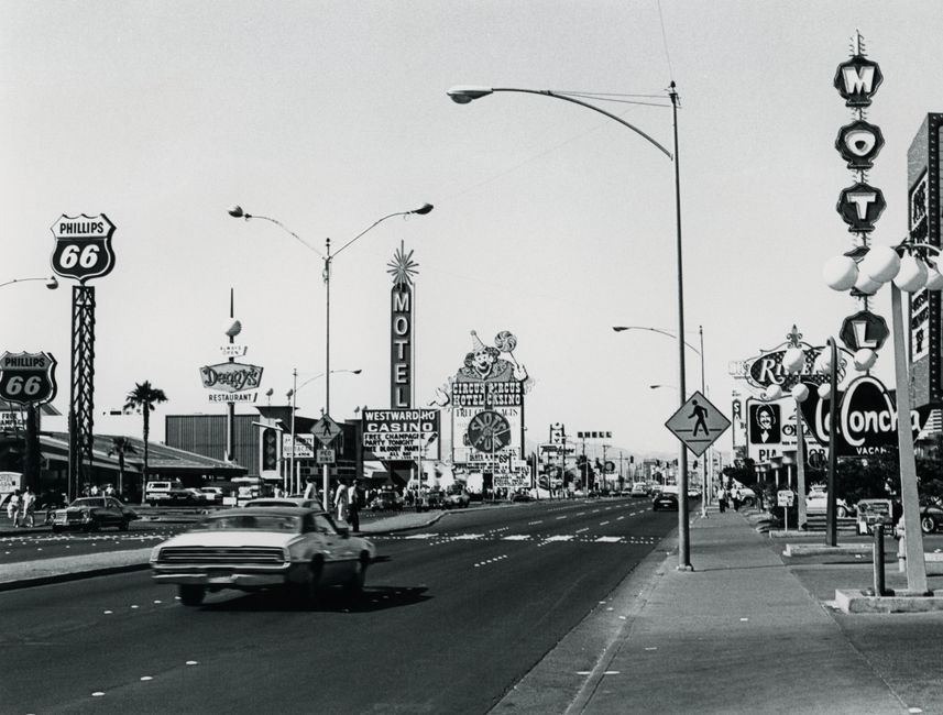 Black and white photo of a bustling Las Vegas street with neon signs and classic cars.