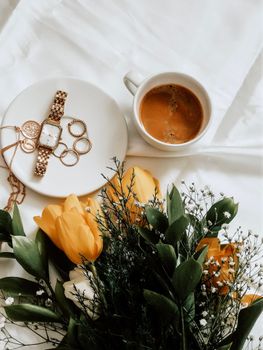 A stylish arrangement of yellow tulips, jewelry, and espresso on white fabric.
