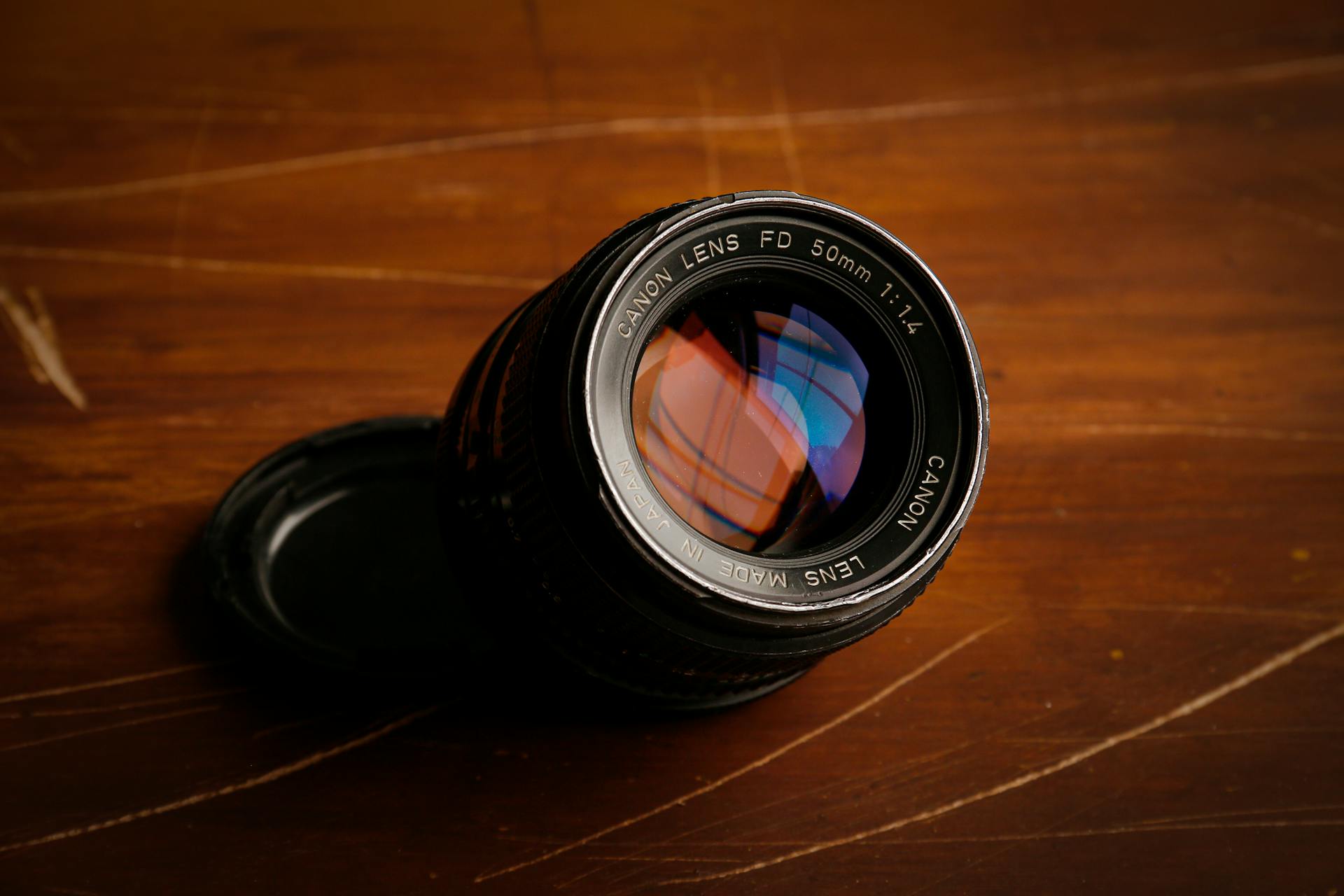 Detailed view of a Canon FD 50mm lens with colorful reflections, placed on a wood surface.