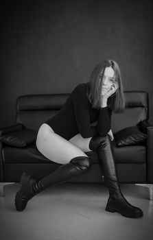 Artistic black and white portrait of a woman in a bodysuit sitting on a sofa.