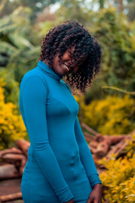 Smiling woman wearing blue dress, enjoying a moment in a vibrant garden setting.