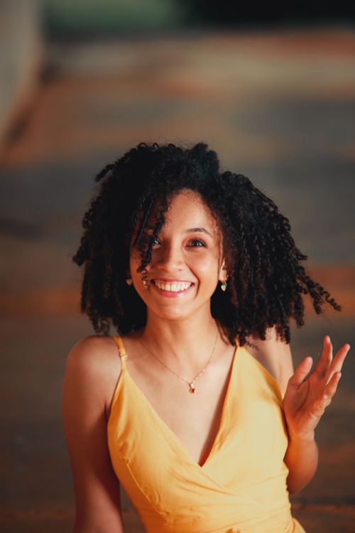 Free Portrait of a happy woman with curly hair in a yellow dress, smiling brightly. Stock Photo