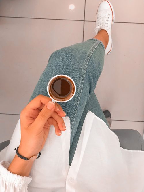 Free Enjoying a hot cup of coffee with denim jeans and white sneakers, captured from above. Stock Photo