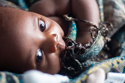 Adorable close-up portrait of a baby with expressive eyes wrapped in patterned fabric.