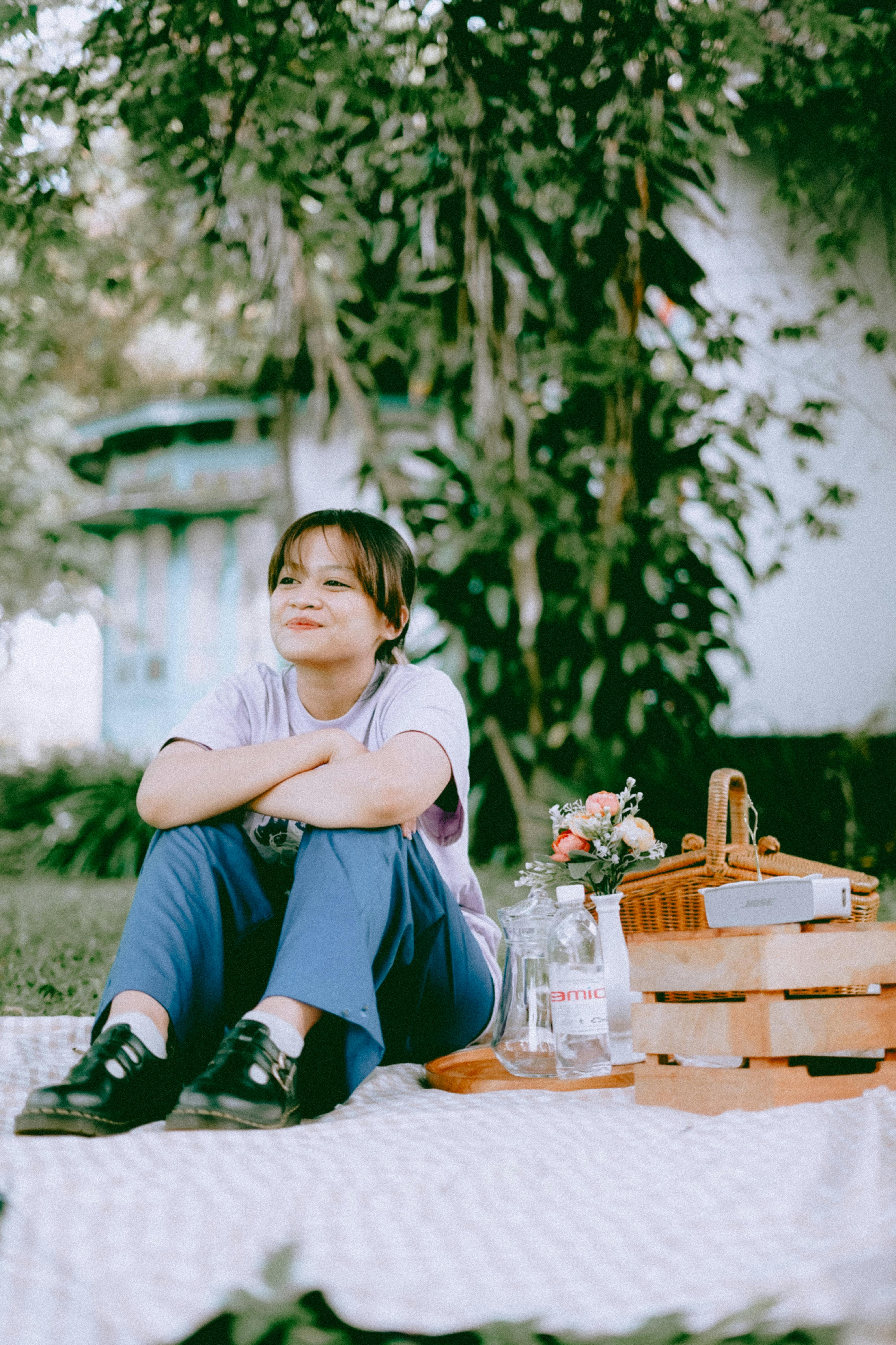 A girl sits on a picnic blanket outdoors, smiling and enjoying the day.