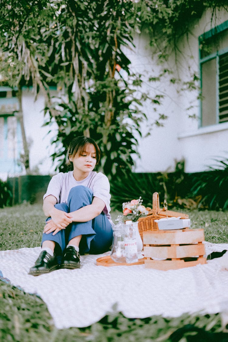 Girl In White T-Shirt And Blue Pants Sitting On A Picnic Rug