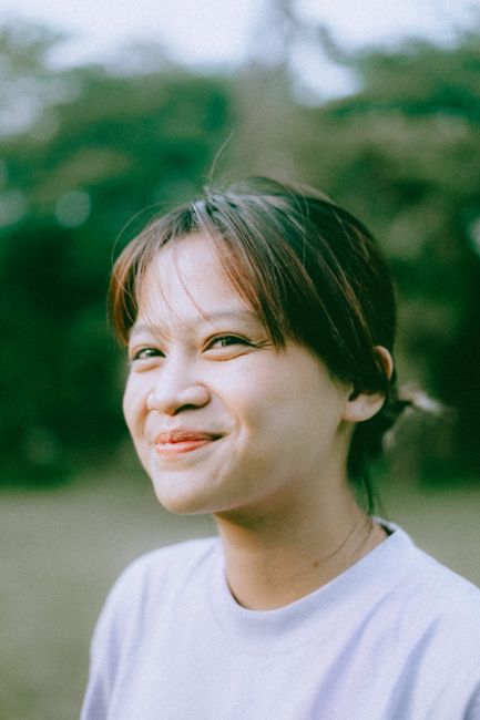A young woman smiling warmly in an outdoor setting, exuding happiness and joy.