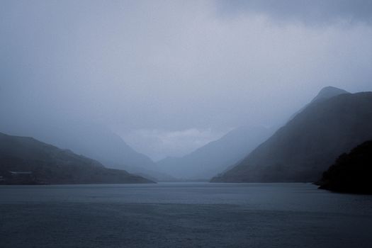 Serene misty landscape of mountains and lake in Wales, creating a tranquil and moody ambiance.