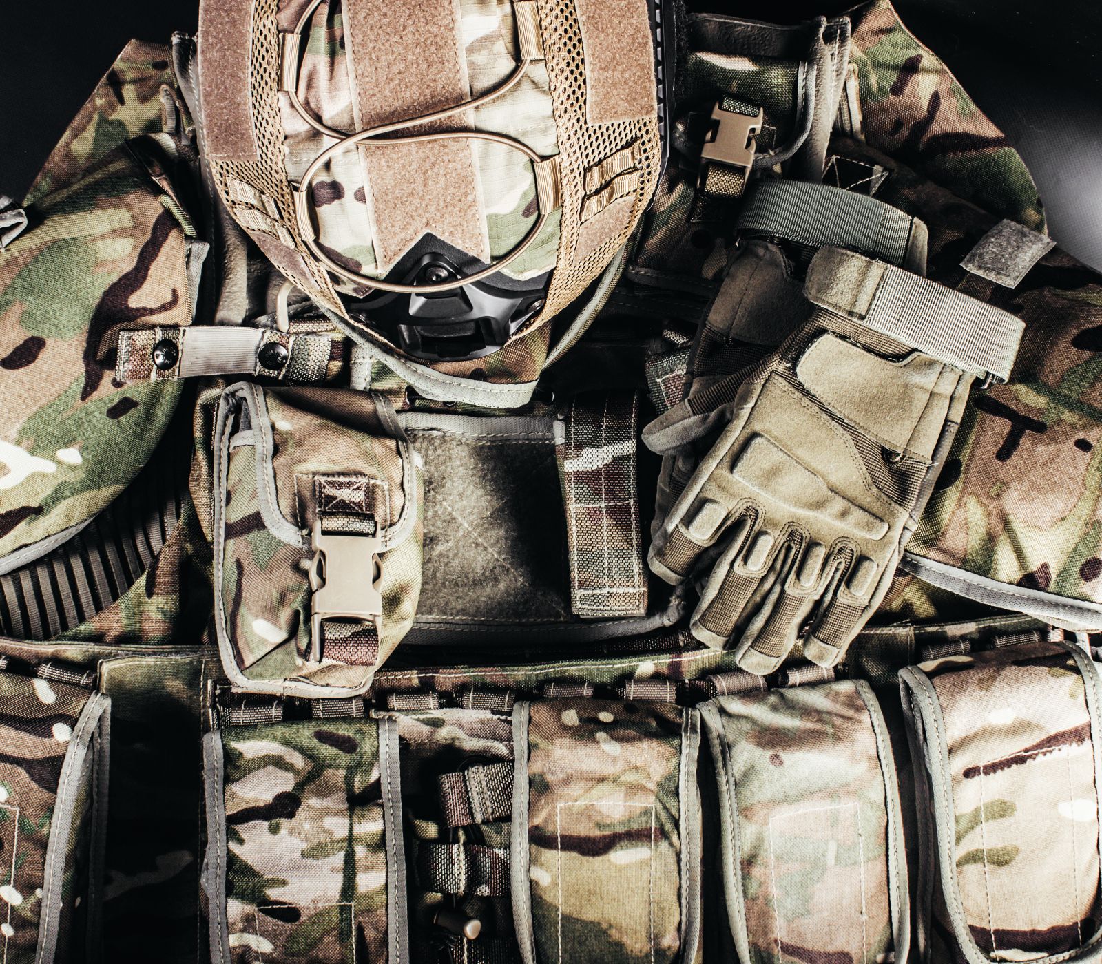 Tactical gear including a camouflage helmet and gloves laid out on the ground for equipment inspection.